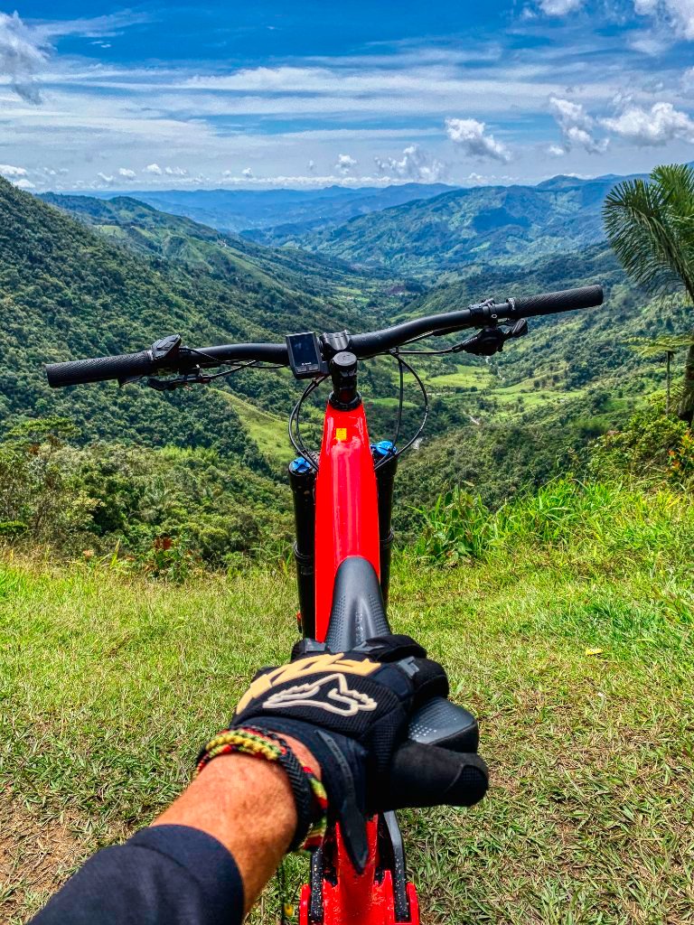 Mountain bike handlebars at the Guatapé River canyon viewpoint, with the forested valley falling away below