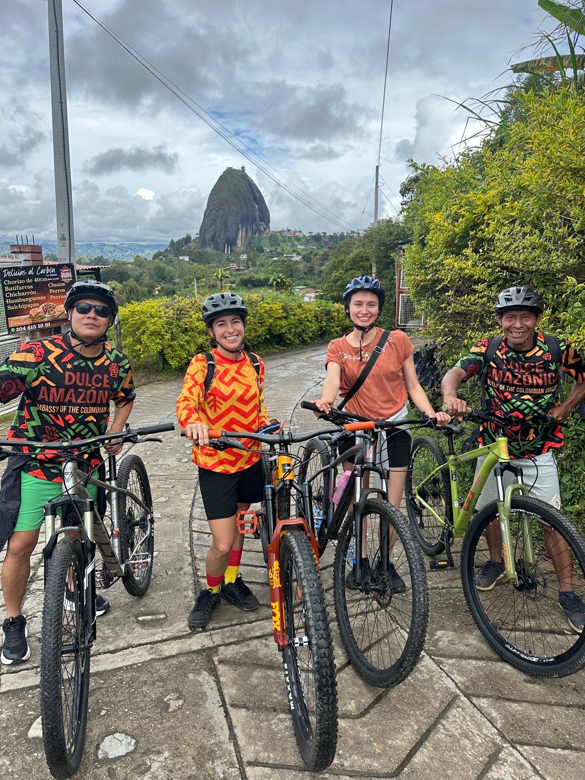 Four riders with MBC mountain bikes and helmets ready to depart, La Piedra del Peñol in the background