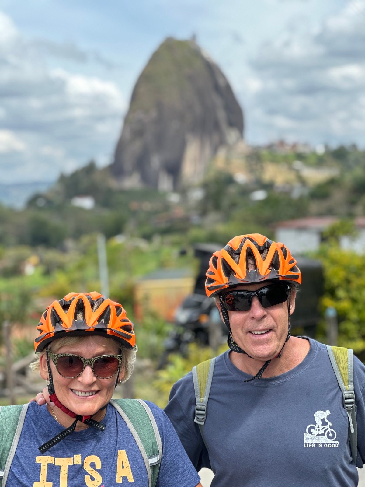 Two riders in helmets with La Piedra del Peñol behind them