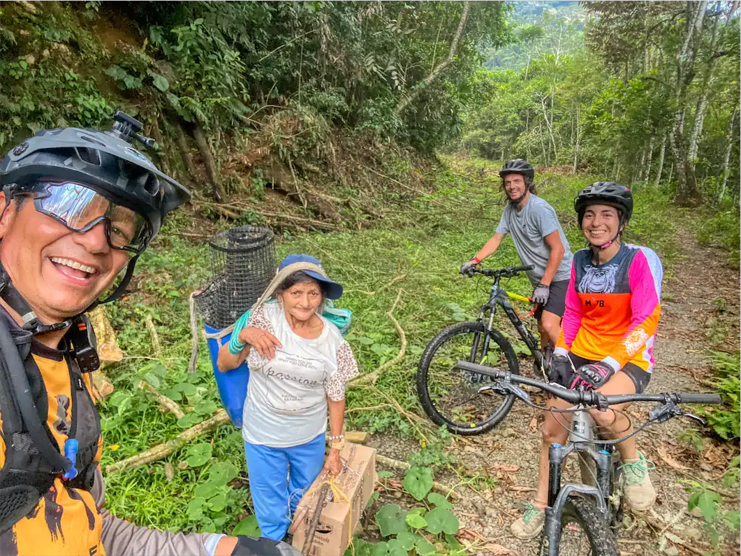 Mountain bikers pausing to greet a local resident carrying a load on a rural forest track