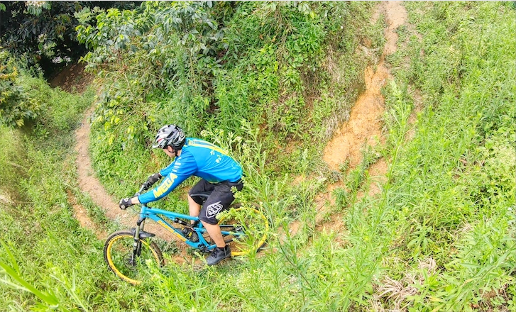Mountain biker leaning through a tight grassy singletrack switchback in green highland terrain